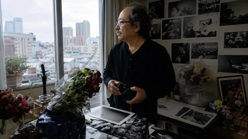 Nobuyoshi Araki dans son atelier tokyoïte entouré de photographies en noir et blanc et de fleurs