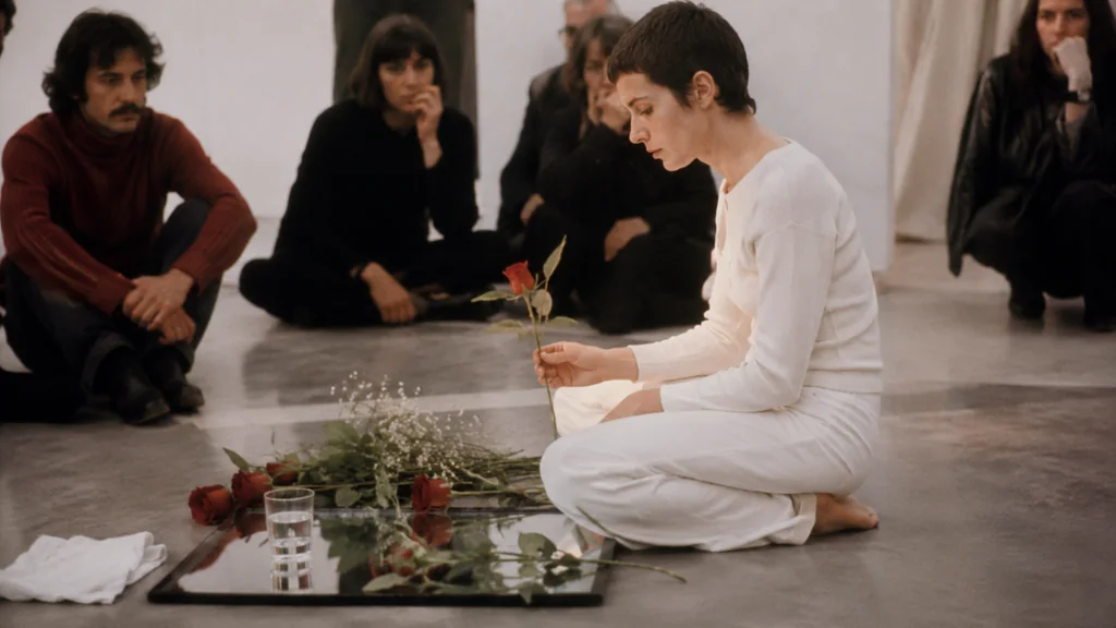 Performance artistique inspirée de l’univers de Gina Pane avec une femme en blanc, des roses et des spectateurs en galerie.