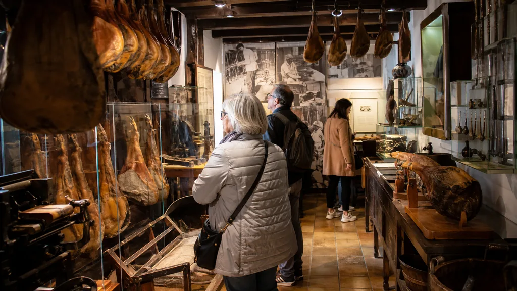 Visiteurs découvrant des jambons affinés, des outils anciens et l’histoire de la charcuterie dans un petit musée de Bayonne.