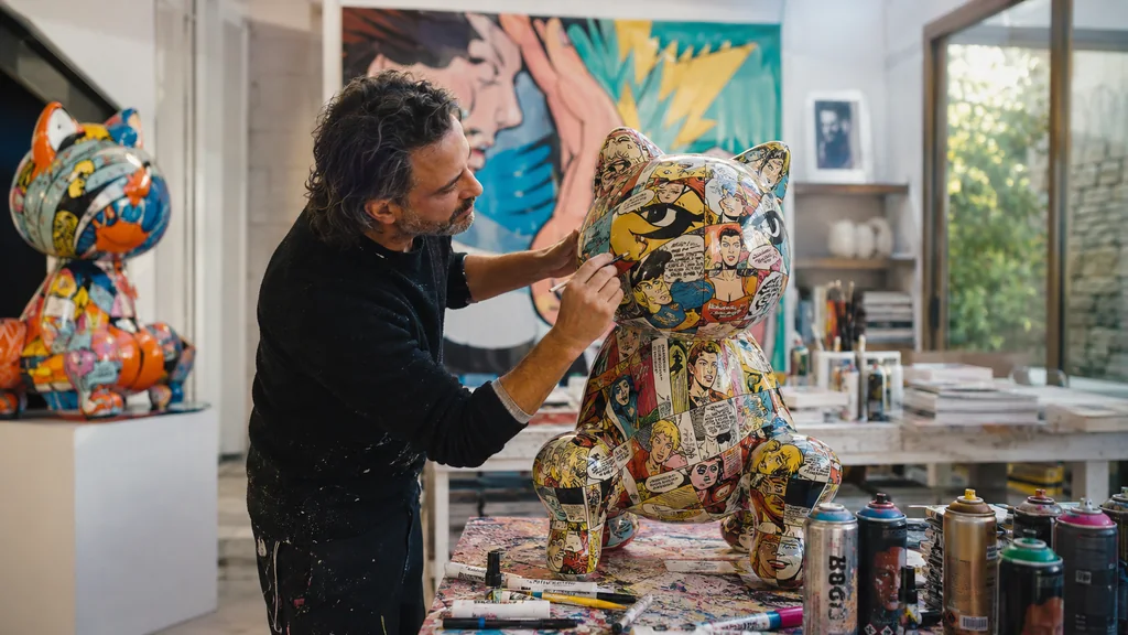 Artiste travaillant sur une sculpture colorée recouverte de fragments de bandes dessinées dans un atelier contemporain.